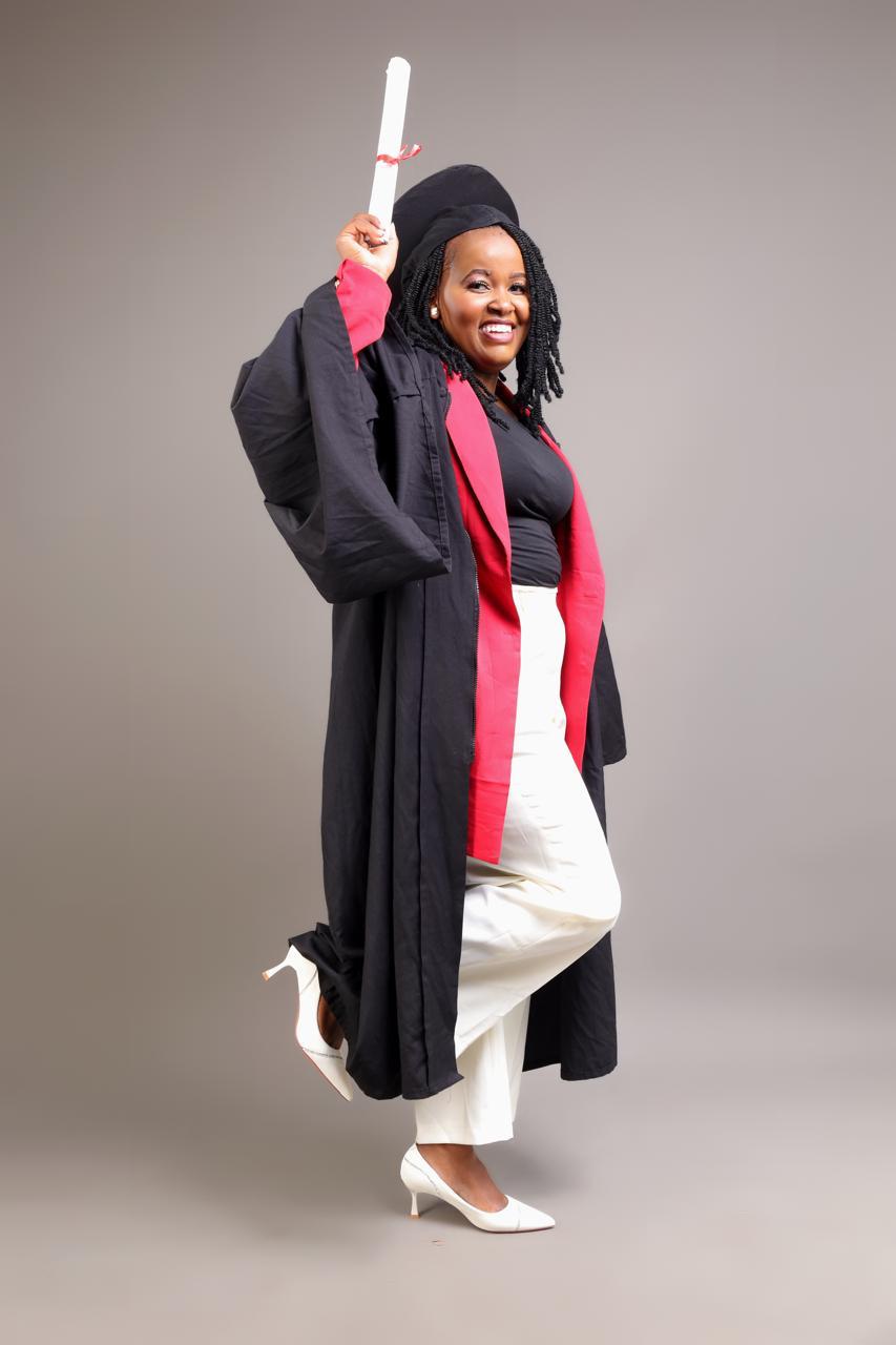 Joy Wanjiku in cap and gown, holding her rolled degree certificate